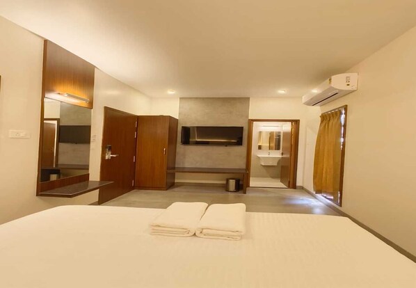 A hotel room with a bed, a mirror, a TV, a sink, and an air conditioning unit.