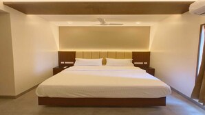A large bed with a wooden headboard, two bedside tables, and a ceiling fan. - Arthana Grand Inn (Udumalaipettai)