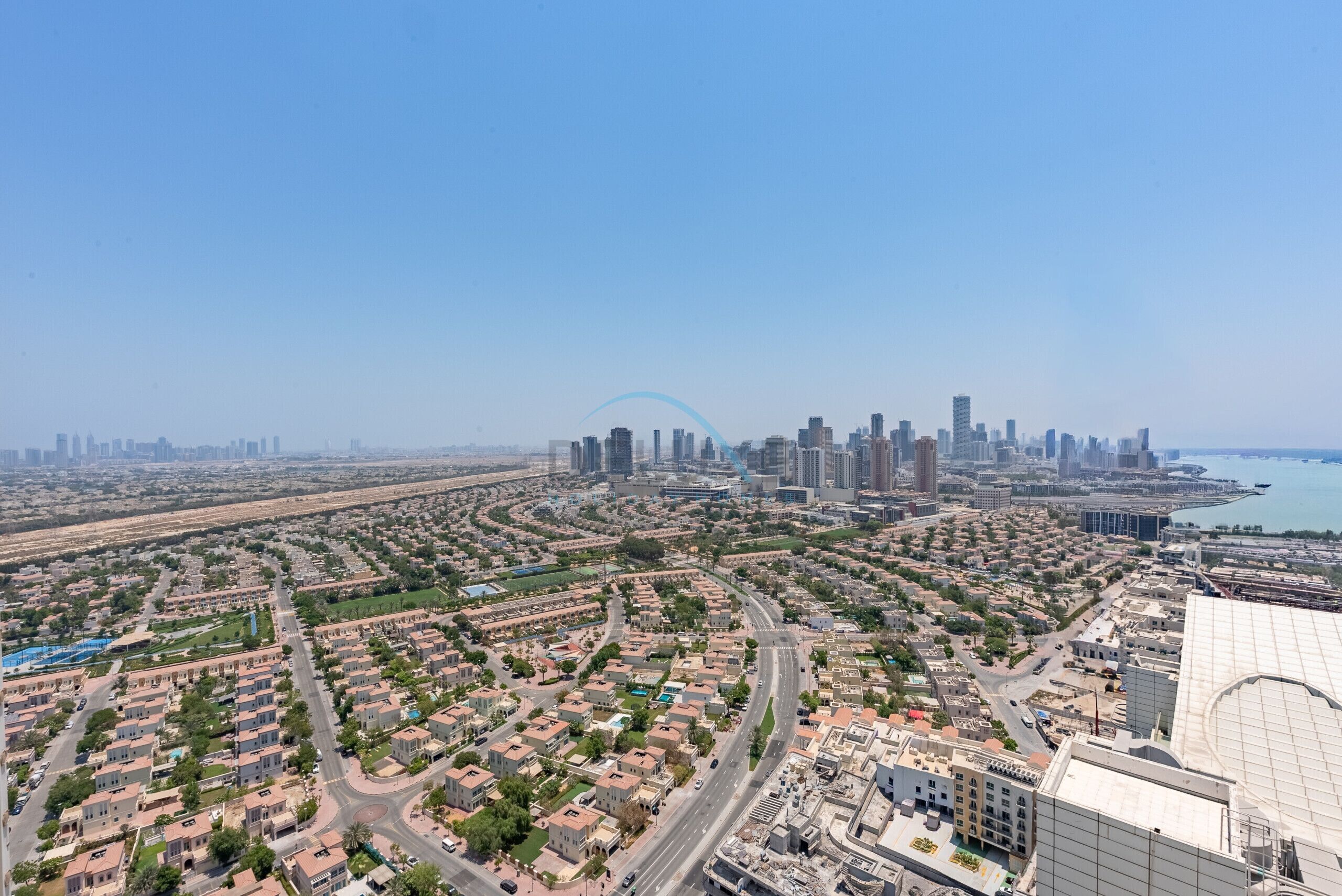 Un quartier résidentiel caractérisé par un tracé de rues sinueux, un bâtiment imposant surmonté d’une structure en forme de dôme, et une vue lointaine sur la silhouette de la ville, avec ses nombreux immeubles de grande hauteur.