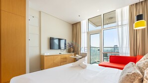 A hotel room with a large bed, a TV, a desk, and a view of the city. - Top-Floor Studio Near a Park and Just Minutes by Car from the Mall (Dubai)