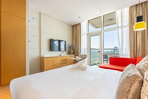 Ein Hotelzimmer mit einem großen Bett, einem Fernseher, einem Schreibtisch und Blick auf die Stadt.