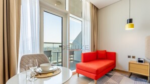 A modern hotel room with a red sofa, a small table with a bowl and glasses, a yellow pendant light, and a view through a glass door. - Top-Floor Studio Near a Park and Just Minutes by Car from the Mall (Dubai)