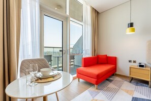 Ein modernes Hotelzimmer mit einem roten Sofa, einem kleinen Tisch mit einer Schale und Gläsern, einer gelben Pendelleuchte und Blick durch eine Glastür.