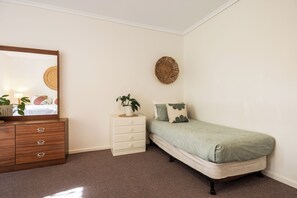 A bedroom with a bed, a dresser, a mirror, a wall hanging, and a plant. - Barossa Suites (Tanunda)