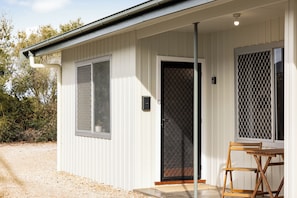 A small, single-story building with a white exterior, a black door, and a window with a metal screen.