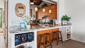 A kitchen with wooden cabinets, a marble countertop, a built-in speaker system, and a bar stool. - Kksr#1301 Direct Oceanfront, Best North Corner Top Floor Location (KAILUA KONA)