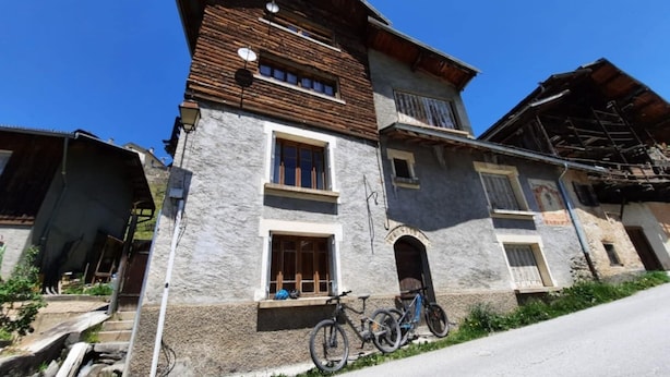 Un edificio de dos pisos con fachada de piedra, un balcón y una bicicleta estacionada frente a él.