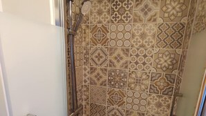 Ducha con cabezal de ducha manual y cabezal de ducha tipo lluvia montado en la pared, rodeada de baldosas con diseños.
