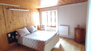 Un dormitorio con techo de madera, una cama con ropa de cama estampada, una silla y un pequeño armario.