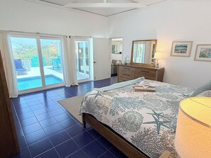 A bedroom with a bed, a dresser, a mirror, and a view of a pool through a sliding door. - Private 3 Bedroom Villa with Pool, Central A/C & Ocean Views in Chocolate Hole, St. John, USVI (St John)
