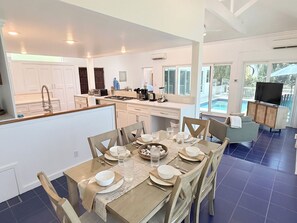 A modern kitchen with white cabinets, a dining area with a table set for four, and a living area with a sofa and TV. - Private 3 Bedroom Villa with Pool, Central A/C & Ocean Views in Chocolate Hole, St. John, USVI (St John)