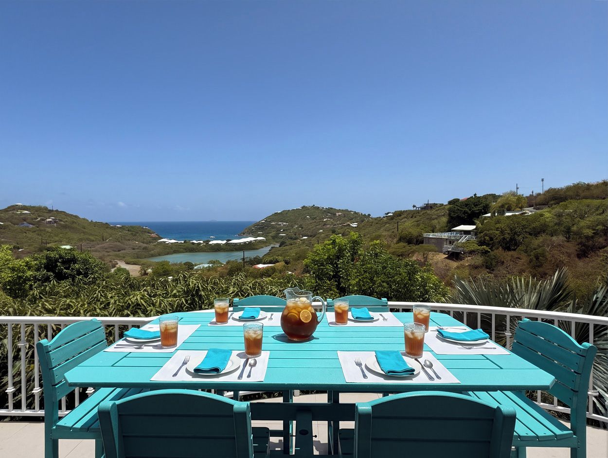 Mesa para cuatro personas con una jarrón y vasos de té helado, con vista a un paisaje costero.