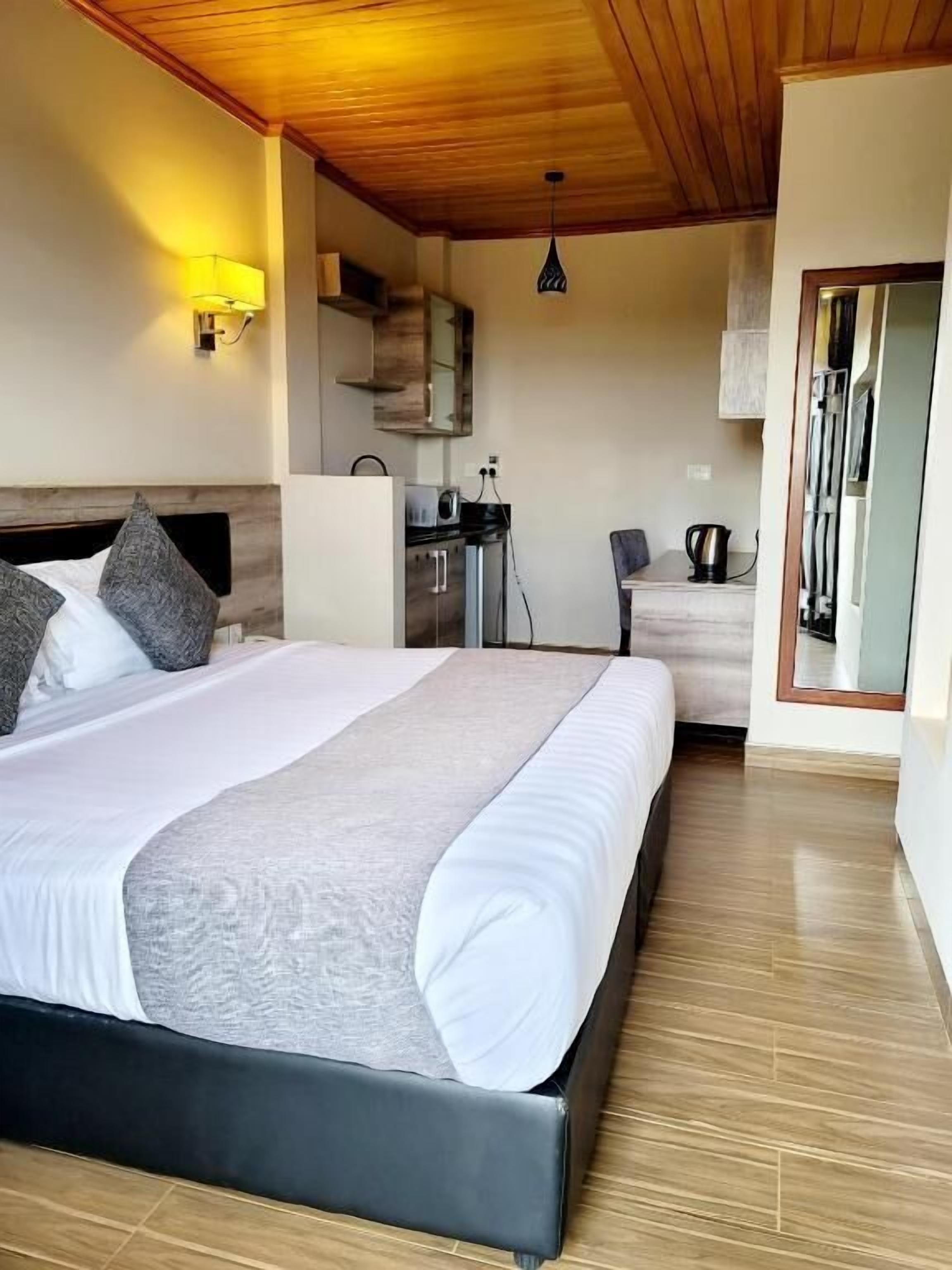 Habitación de hotel con una cama grande, techo de madera, kitchenette y un espejo.