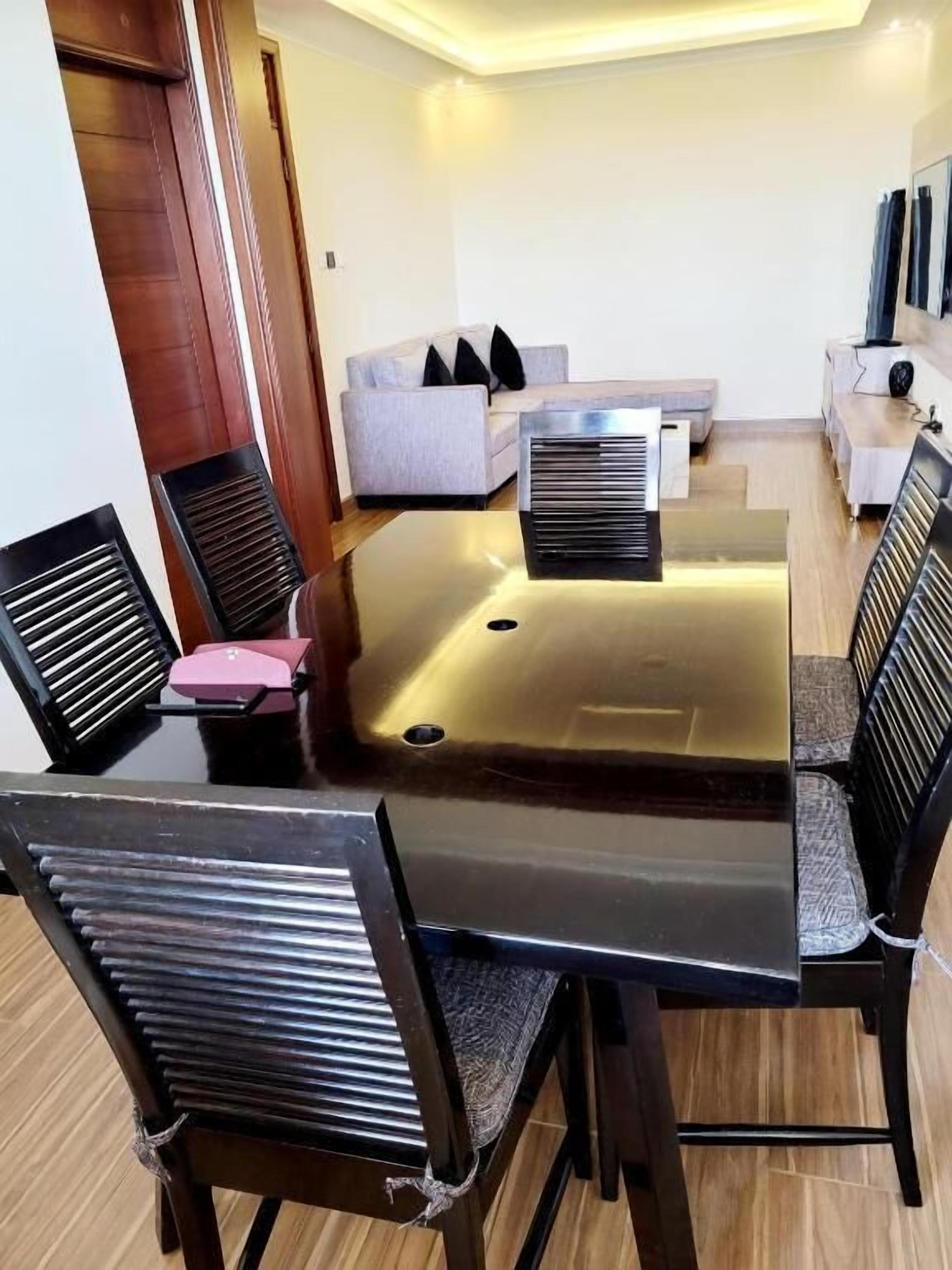 Un comedor con una mesa de vidrio, sillas negras, un sofá y un televisor en la pared.
