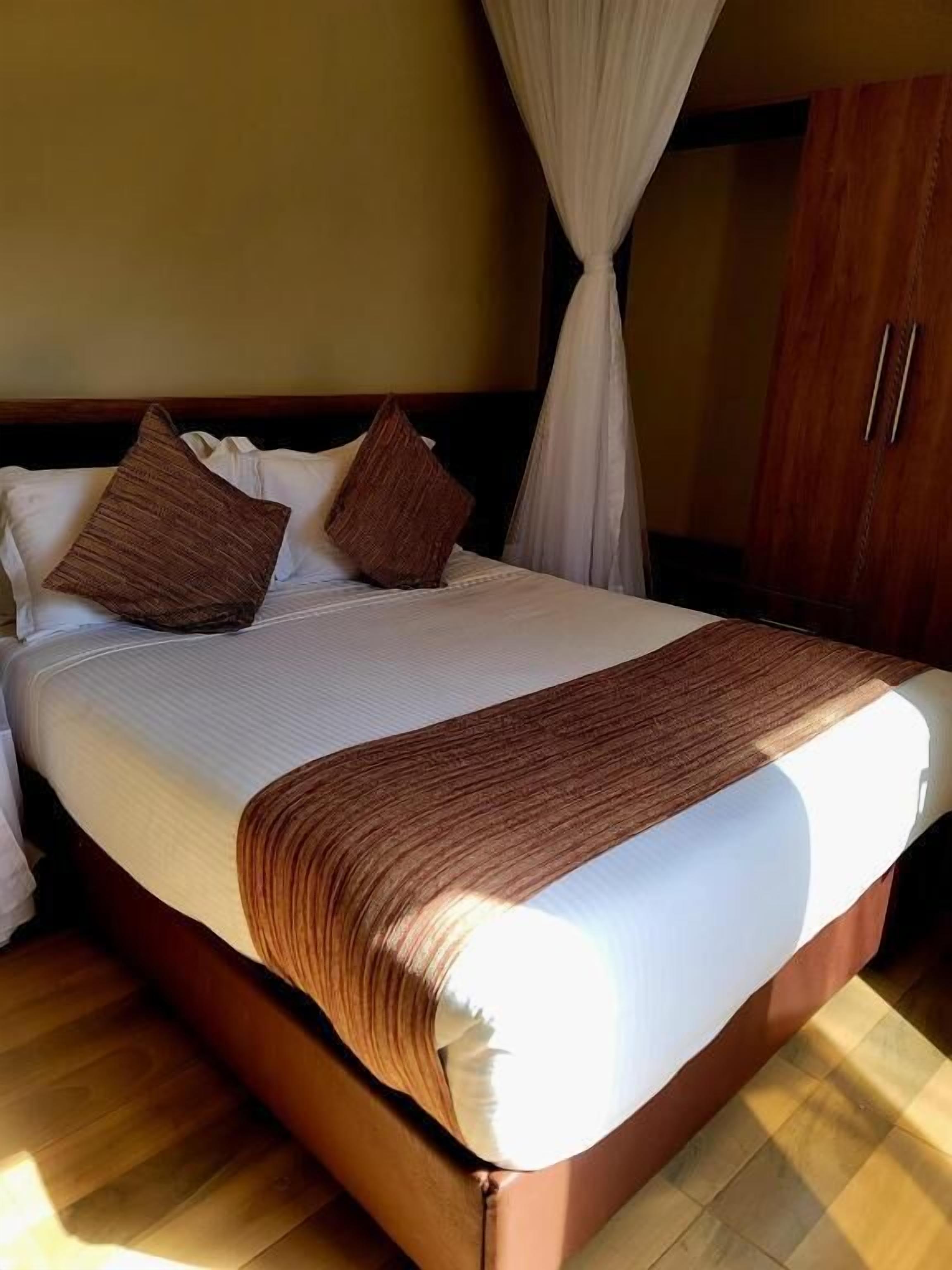 A bed with a white mattress, brown pillows, and a brown throw blanket.