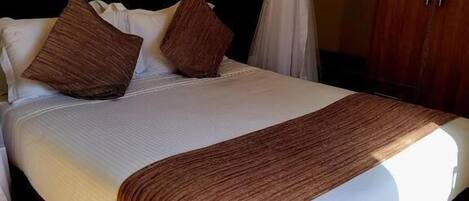 A bed with a white mattress, brown pillows, and a brown throw blanket.