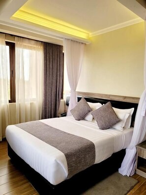 Habitación de hotel con una cama grande, cabecero de madera y vistas al exterior a través de la ventana.