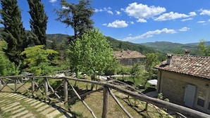A rural setting with a wooden fence, a house with a tiled roof, and a mountainous landscape in the background.
