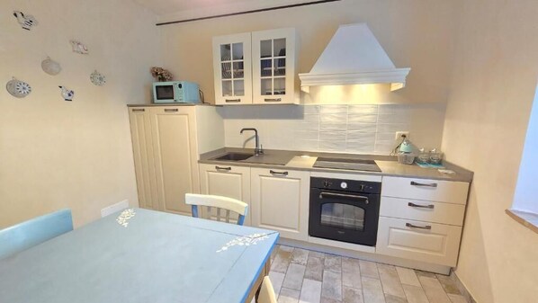 A compact kitchen with a dining area, white cabinetry, a microwave, and a stove.