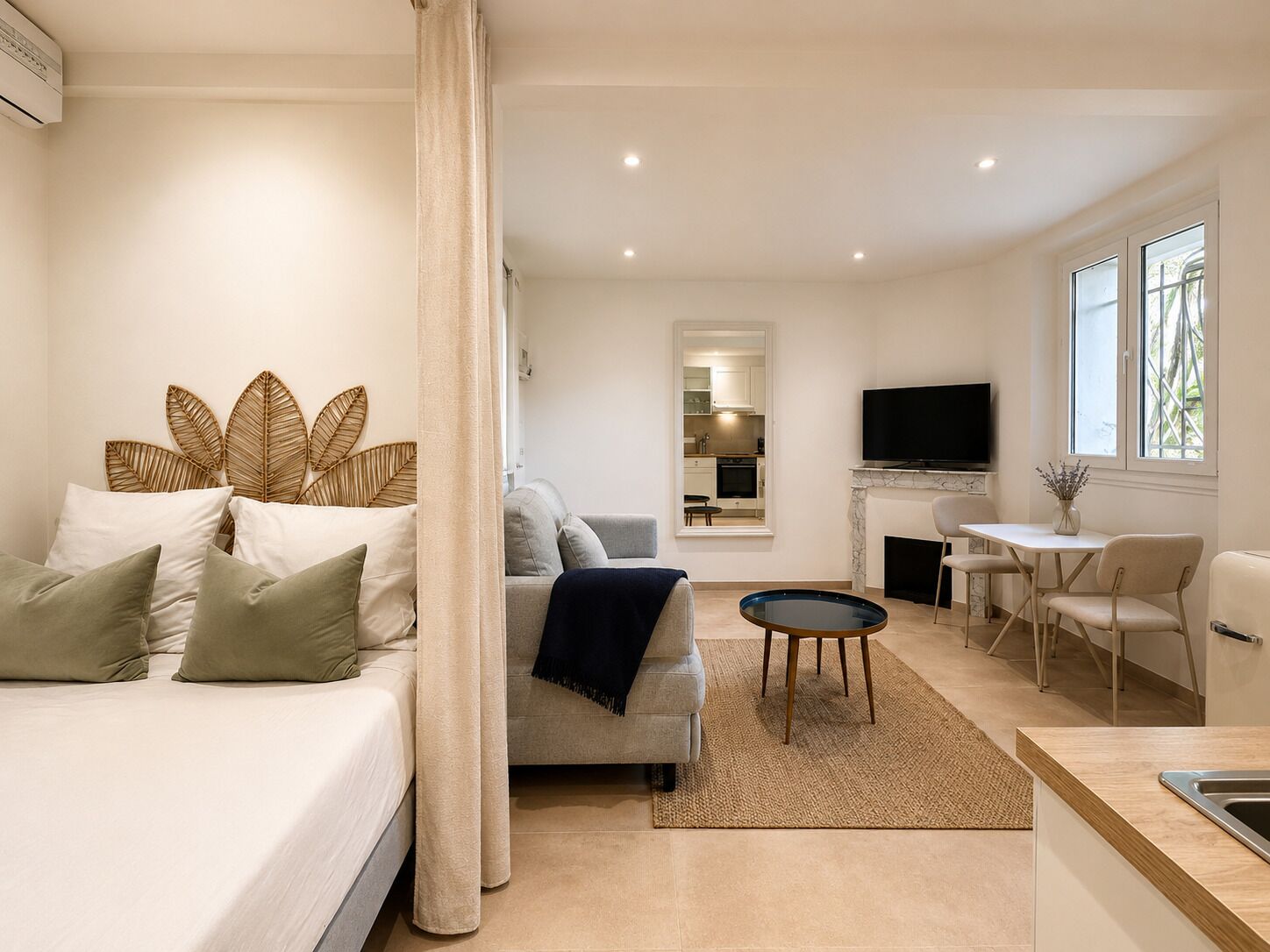 A modern hotel room with a bed, a sofa, a TV, a dining area, and a kitchen.