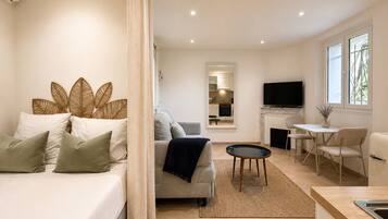 A modern hotel room with a bed, a sofa, a TV, a dining area, and a kitchen.