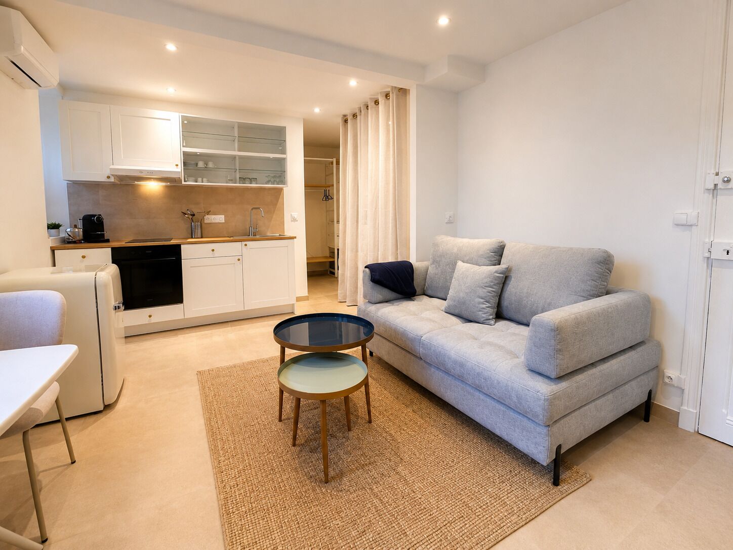 Un espace de vie compact comprenant un coin cuisine, un canapé, une petite table et une porte.