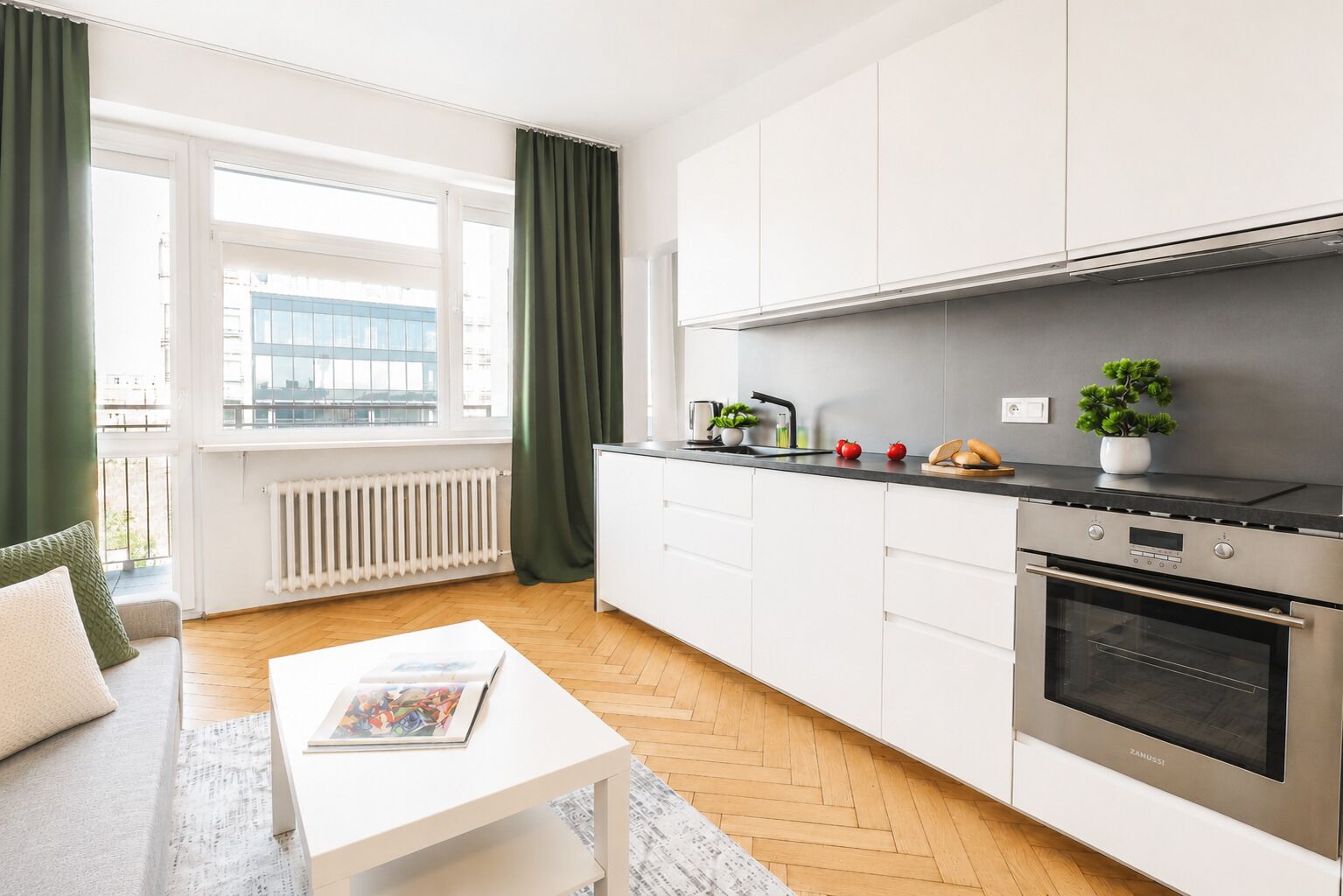 Una cocina moderna con armarios blancos, horno empotrado y ventana con cortinas.