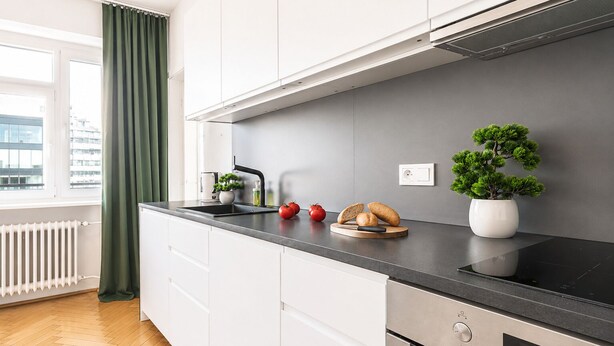 A modern kitchen with a black countertop, white cabinets, a built-in oven, and a window with a view of buildings. - Lumina 2-room Apart with Balcony Center (Warszawa)