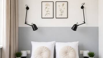 A neatly made bed with white linens, two wall-mounted lamps, and a framed botanical print above it.
