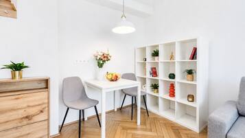 A modern living room with a white dining table, two grey chairs, a white bookshelf, and a herringbone-patterned wooden floor.