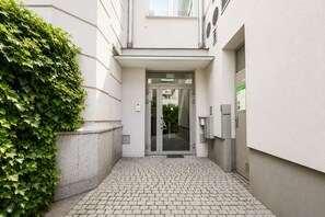 Ein Gebäudeeingang mit Glastür, befestigtem Weg und einer grünen Hecke.