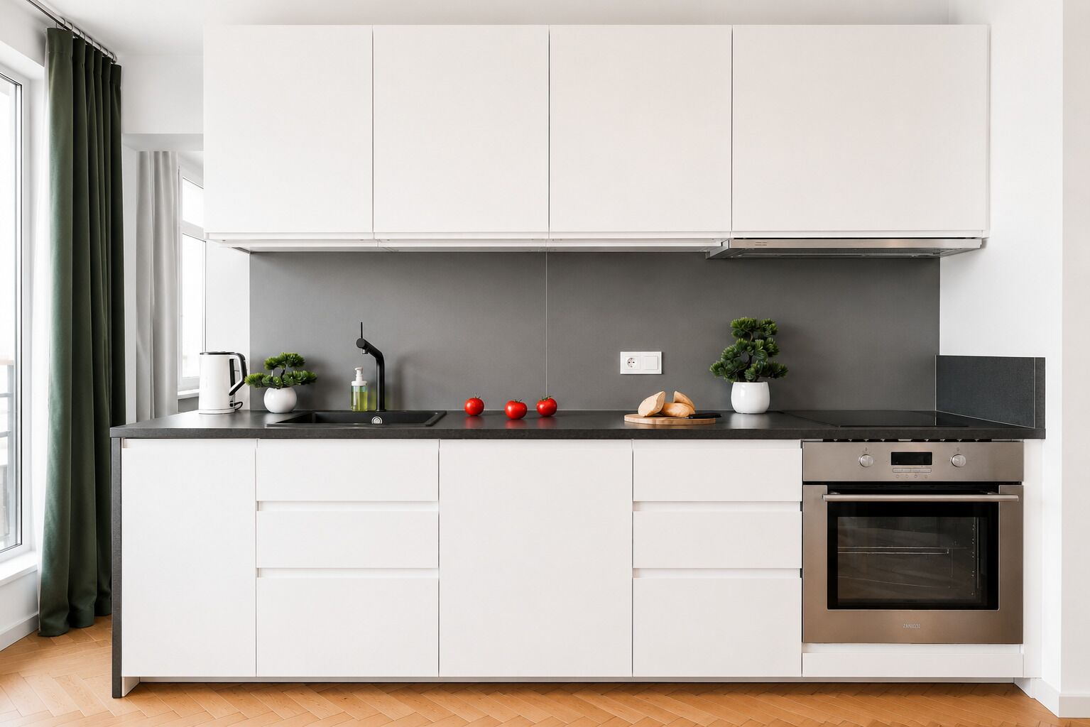 Eine moderne Küche mit weißen Schränken, einer schwarzen Arbeitsplatte, einem eingebauten Backofen und einem Fenster mit Vorhängen.