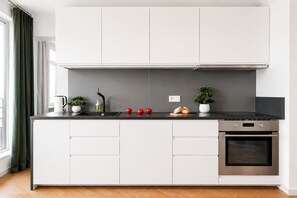 Eine moderne Küche mit weißen Schränken, einer schwarzen Arbeitsplatte, einem eingebauten Backofen und einem Fenster mit Vorhängen.