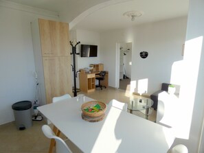 Ein moderner Wohnraum mit Essbereich, einem Holzschrank, einem Fernseher und einem Flur, der zu einem Kleiderschrank führt.