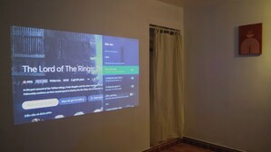 A projection screen displaying information about 'The Lord of the Rings' film, a room with a wooden floor, a curtain, and a piece of abstract art on the wall.