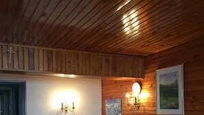 A wooden-paneled room with a table and chairs, two wall-mounted lights, and a framed picture. - 100 M² DUPLEX "SPECIAL OFFER" IN THE HEART OF LES CARROZ—Sleeps 9, 3 bedrooms, 2 bathrooms (Arâche -La-Frasse)