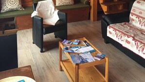 A cozy cabin interior with a wooden wall, a staircase, a sofa, a chair, and a coffee table with magazines. - 100 M² DUPLEX "SPECIAL OFFER" IN THE HEART OF LES CARROZ—Sleeps 9, 3 bedrooms, 2 bathrooms (Arâche -La-Frasse)