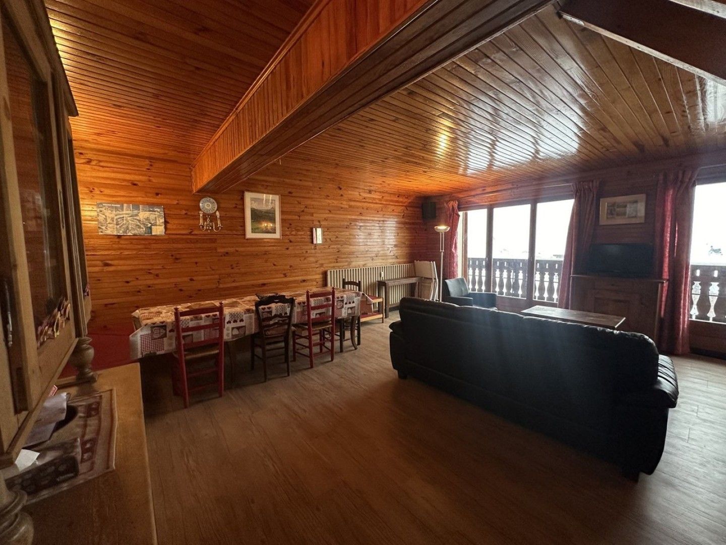 A wooden interior with a dining area, sofa, and a view through a window.