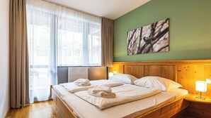 Una camera d'albergo con un letto in legno, un termosifone, una finestra con tende e una parete verde decorata con un'opera d'arte che ricorda il marmo.