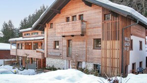 Un chalet in legno con un balcone, un cartello con su scritto 'WILDBACHHOF' e un paesaggio innevato.