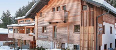 A wooden chalet with a balcony, a sign reading 'WILDBACHHOF,' and a snow-covered landscape.