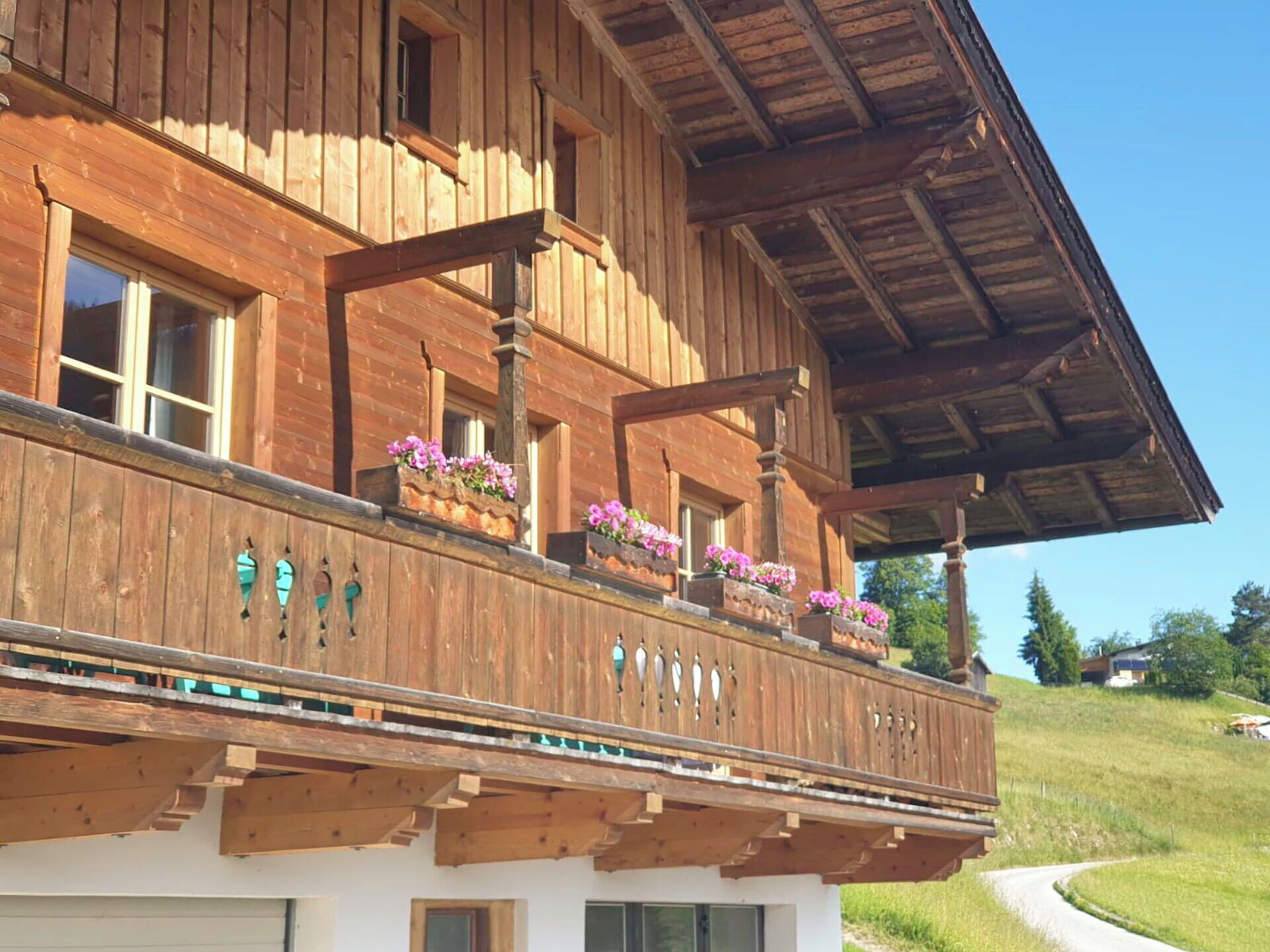 Un chalet in legno con un balcone decorato da fioriere, un tetto spiovente e vista su un paesaggio verde.