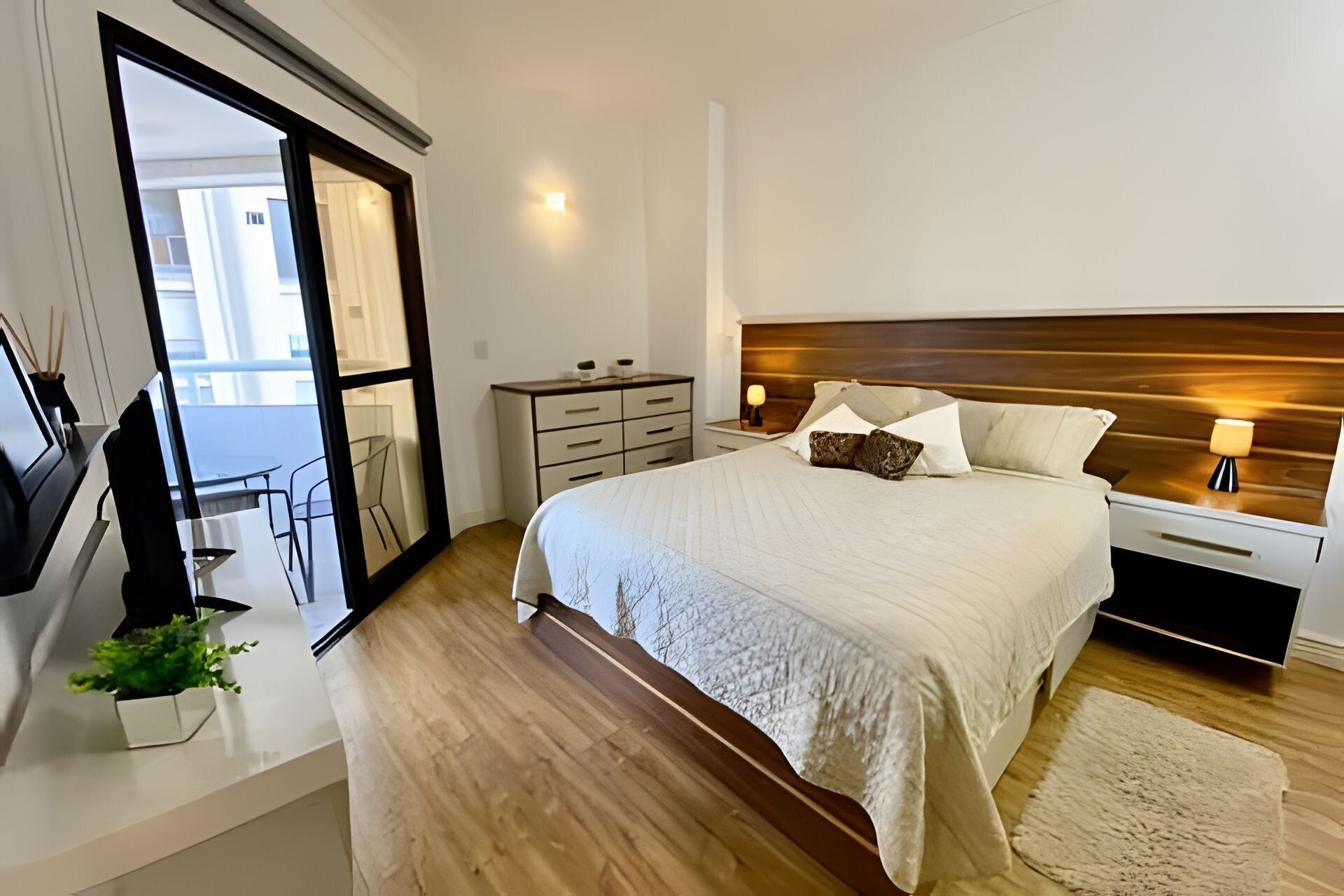 A modern bedroom with a large bed, bedside tables, a TV, and a view of the outside.
