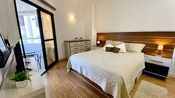 Un dormitorio moderno con una cama grande, mesitas de noche, televisor y vistas al exterior.