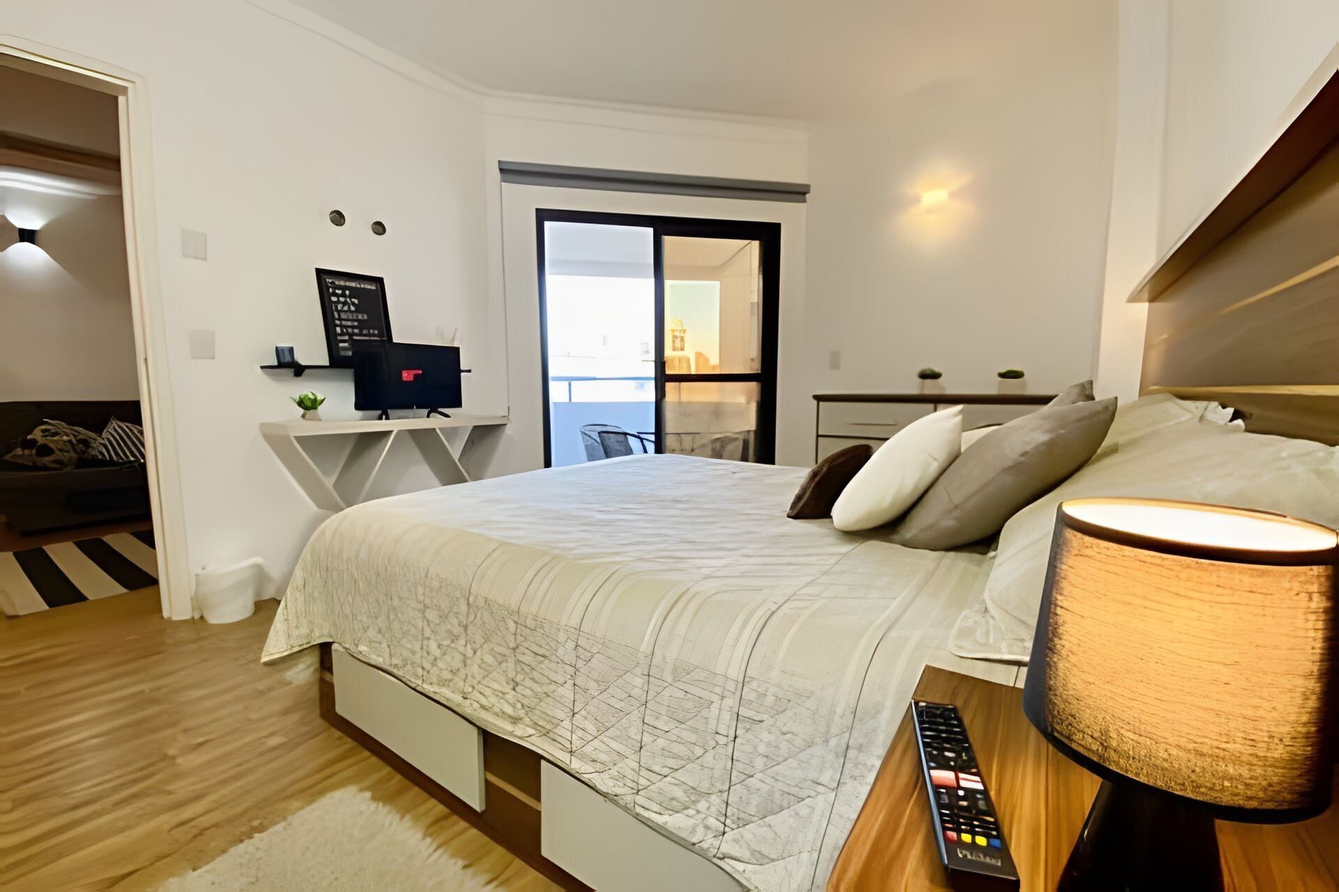 Un dormitorio moderno con cama, mesita de noche, lámpara y escritorio con ordenador.