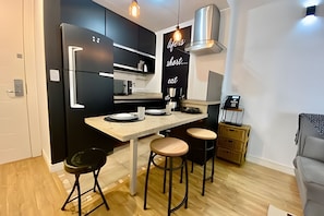 A modern kitchen with black cabinets, a stainless steel range hood, and a bar area with stools. - SHB Moderno e Sofisticado Frente a Praia (Santos)