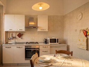 Eine Küche mit Gasherd, Backofen, Mikrowelle, hängendem Kochgeschirr und einer Uhr an der Wand.