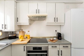 A modern kitchen with white cabinets, a built-in oven, a coffee maker, and a cutting board with lemons. - A calm, classic two bedroom home in Tetuán, with parquet floors, a decorative fireplace, and a small balcony. Elegant and comfortable for daily life in Madrid. (Madrid)