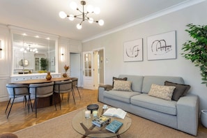 A modern living room with a grey sofa, a glass coffee table, and a dining area with a wooden table and chairs. - A calm, classic two bedroom home in Tetuán, with parquet floors, a decorative fireplace, and a small balcony. Elegant and comfortable for daily life in Madrid. (Madrid)