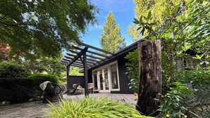 A covered outdoor seating area with chairs, a pergola, and a view of a house with a glass door.